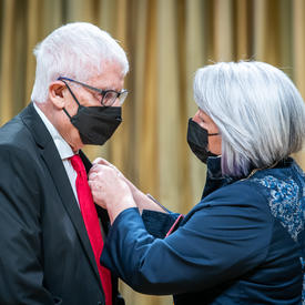 The Governor General is placing a pin on alcides lanza’s suit jacket.