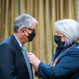 The Governor General is placing a pin Nadir H. Mohamed’s suit jacket.