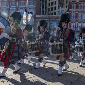 Les tambours, vêtus d'uniformes militaires composés d'un kilt et de tartan, marchent et jouent.