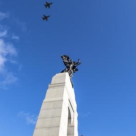 Five airplanes against a bright blue sky are flying above the National War Memorial. 