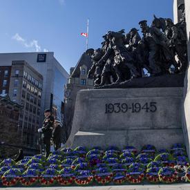Des centaines de couronnes sont déposées à la base du Monument commémoratif de guerre du Canada.  Deux sentinelles se tiennent au garde à vous.