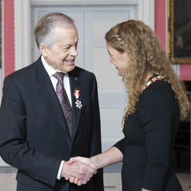 The Governor General, Julie Payette, shakes Howard Gimbel's hand as they speak.  Both are wearing their Order of Canada insignias.