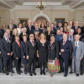 The Governor General, Julie Payette, stands surrounded by 41 recipients of the Order of Canada on the stairs in the front foyer of Rideau Hall. 
