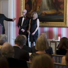 Lori Saint-Martin and Paul Gagné stand on stage.  The Governor General, Julie Payette, sits to their right.  M. Charles Tisseyre stand at the podium to their right. 
