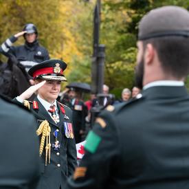 The Governor General Julie Payette, wearing an army uniform, salutes.  Servicemen and women stand in the foreground.