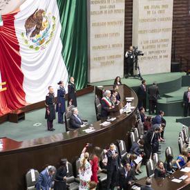 His Excellency Andrés Manuel López Obrador is standing on a stage addressing the members of congress and guests. 