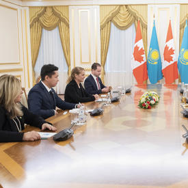 A group of 8 people are seated around a large oblong table.  The Governor General, Julie Payette, and His Excellency Nursultan Nazarbayev, President of Kazakhstan are seated in the middle. In the background are Canadian and Kazakhstani flags.