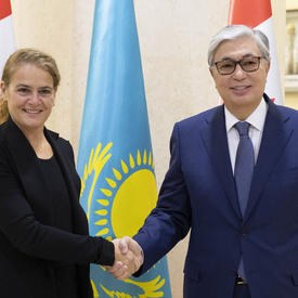 The Governor General shakes the hand of His Excellency Kassym-Jomart Tokayev, Chairman of the Senate of the Parliament of the Republic of Kazakhstan.  They smile for the camera.  Behind them are Canadian and Kazakhstani flags.