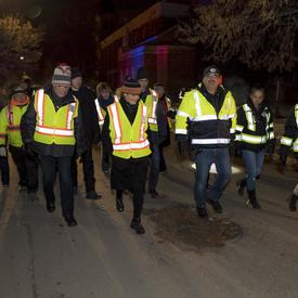 Her Excellency and other volunteers are walking on the street wearing reflective vests. 
