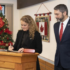The Governor General is signing a guest book.  Sandy Silver, Premier of Yukon, stands next to her. 