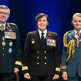 Recipient Captain(N) Rebecca Louise Patterson stands between the Vice Chief of the Defence Staff, Lieutenant-  General Paul Wynnyk (on the left) and Her Excellency the Right Honourable Julie Payette (on the right).