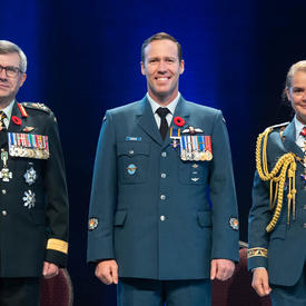 Recipient Warrant Officer Aaron David Bygrove stands between the Vice Chief of the Defence Staff, Lieutenant-  General Paul Wynnyk (on the left) and Her Excellency the Right Honourable Julie Payette (on the right).