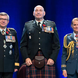 Recipient Major James Edward Rene MacInnis stands between the Vice Chief of the Defence Staff, Lieutenant-General   Paul Wynnyk (on the left) and Her Excellency the Right Honourable Julie Payette (on the right).