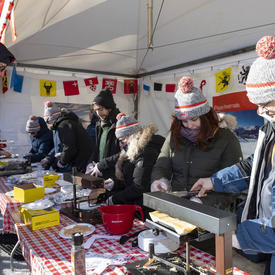 Half a dozen volunteers in winter gear serve raclette to visitors. 