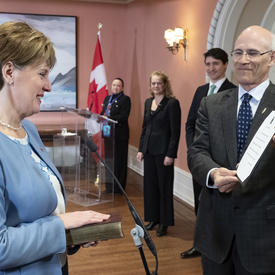 Marie-Claude Bibeau stands in front of the Michael Wernick, clerk of the Privy Council, who holds up the Oath of Office. Her right hand is placed on a Bible.  Behind them stand Prime Minister Justin Trudeau, Governor General Julie Payette and the MC. 