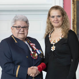Marie-Anne Day Walker-Pelletier shakes the Governor General's hand.  They smile at the camera and are both wearing their Order of Canada insignia.