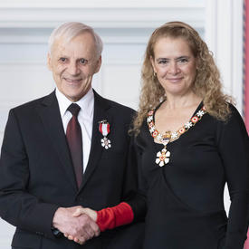 Raymond L. Desjardins shakes the Governor General's hand. They smile at the camera and are both wearing their Order of Canada insignia.