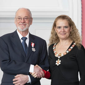 Barry Wellar shakes the Governor General's hand. They smile at the camera and are both wearing their Order of Canada insignia
