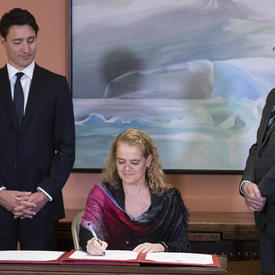 La gouverneure générale signe le livre des serments. Le premier ministre et le greffier du Conseil privé sont a ses côtés. 