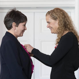 The Governor General pins a medal on Hayley Hesseln's lapel.  They look at each other smiling. 