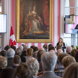 A photo of the room with the Governor General standing at the front.