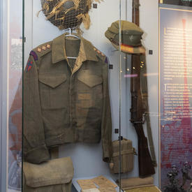 Des éléments de l'uniforme d'un soldat canadien de la Seconde Guerre mondiale sont exposés dans une valise sur un mur.