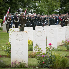 Des rangées de pierres tombales blanches au cimetière de guerre canadien de Bény-sur-Mer pour commémorer le 75e anniversaire du jour J. Les militaires sont alignés à distance.