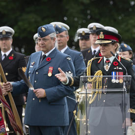 La gouverneure générale Julie Payette, en uniforme de la Force aérienne du Canada, prononce une allocution à une tribune. Elle est entourée de militaires.