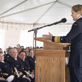 Governor General Julie Payette is seen from her left profile, speaking at a podium, in front of a seated  audience, under a white tent.