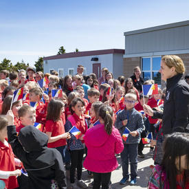 Governor General Julie Payette is outside, on a sunny day, meeting with a large group of elementary school students.