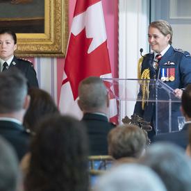 The Governor General delivers remarks at a podium, an aide-de-camp stands nearby.