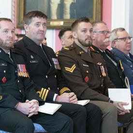 Les récipiendaires de la cérémonie à thème militaire sont assis dans la première rangée et regardent les autres récipiendaires se faire décerner.