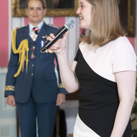 Ms. Molly McGuire sings the national anthem as the Governor General stands in solidarity.
