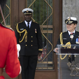 The Governor General delivers a speech at a podium with her aide-de-camp by her side.
