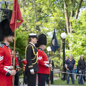 La gouverneure générale se tient entre deux gardes qui observent la Garde de cérémonie avec une admiration silencieuse.