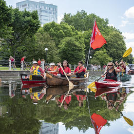 The Governor General is kayaking down the Ottawa canal and other people are accompanying her in canoes. 