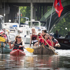 The Governor General is kayaking down the Ottawa canal and other people are accompanying her in canoes. 