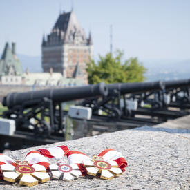 A picture of the Order of Canada Medals, laid out on a stone wall, with cannons and the Chateau Frontenac in the background.