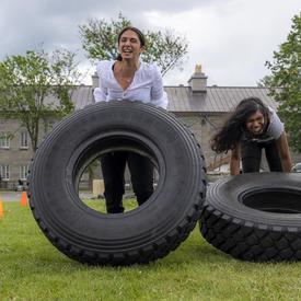 Two women are flipping tires as part of an obstacle course. 