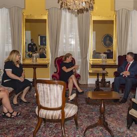The Governor General, Her Honour the Honourable Antoinette Perry, Lieutenant Governor of Prince Edward Island, and the Honourable Dennis King, Premier of Prince Edward Island, sit and discuss with other delegates in a room inside Government House.