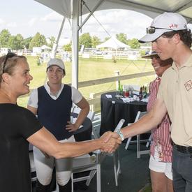 The Governor General shakes hands with a young rider in stands overlooking an equestrian competition course.