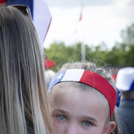 A young girl dressed in Acadian national colours is in her mother’s arms. 