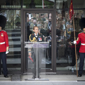 The Governor General delivers remarks at a podium, two ceremonial guards standing solemnly on either side. 
