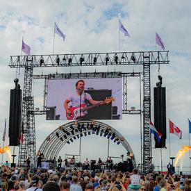 A photo of the main outdoor stage at the commemorative ceremony in Terneuzen, a large crowd surrounds it. 