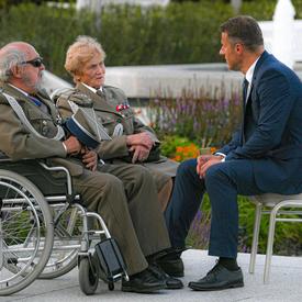 A photo of a man in a suit speaking with two Polish veterans in wheelchairs.