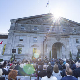 Photo d'une foule assise à l'extérieur de l'entrée principale de Rideau Hall lors d'une cérémonie extérieure de l'Ordre du Canada.