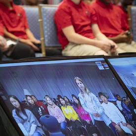 A picture of students seated in the Tent Room of Rideau Hall, with a virtual classroom from Vancouver on a screen.
