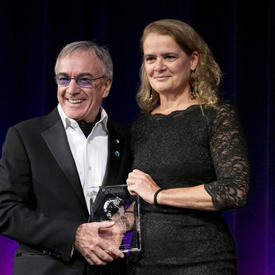 Daniel Lamarre, President of Cirque du Soleil, and Governor General Julie Payette of Canada hold a prize made of transparent glass in their hands.