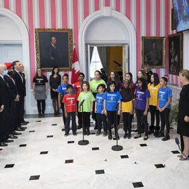 A choir of kids is standing at the front of the room.