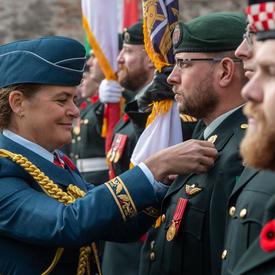 Governor General Julie Payette is adjusting a poppy on the uniform of a member of the Canadian Forces.